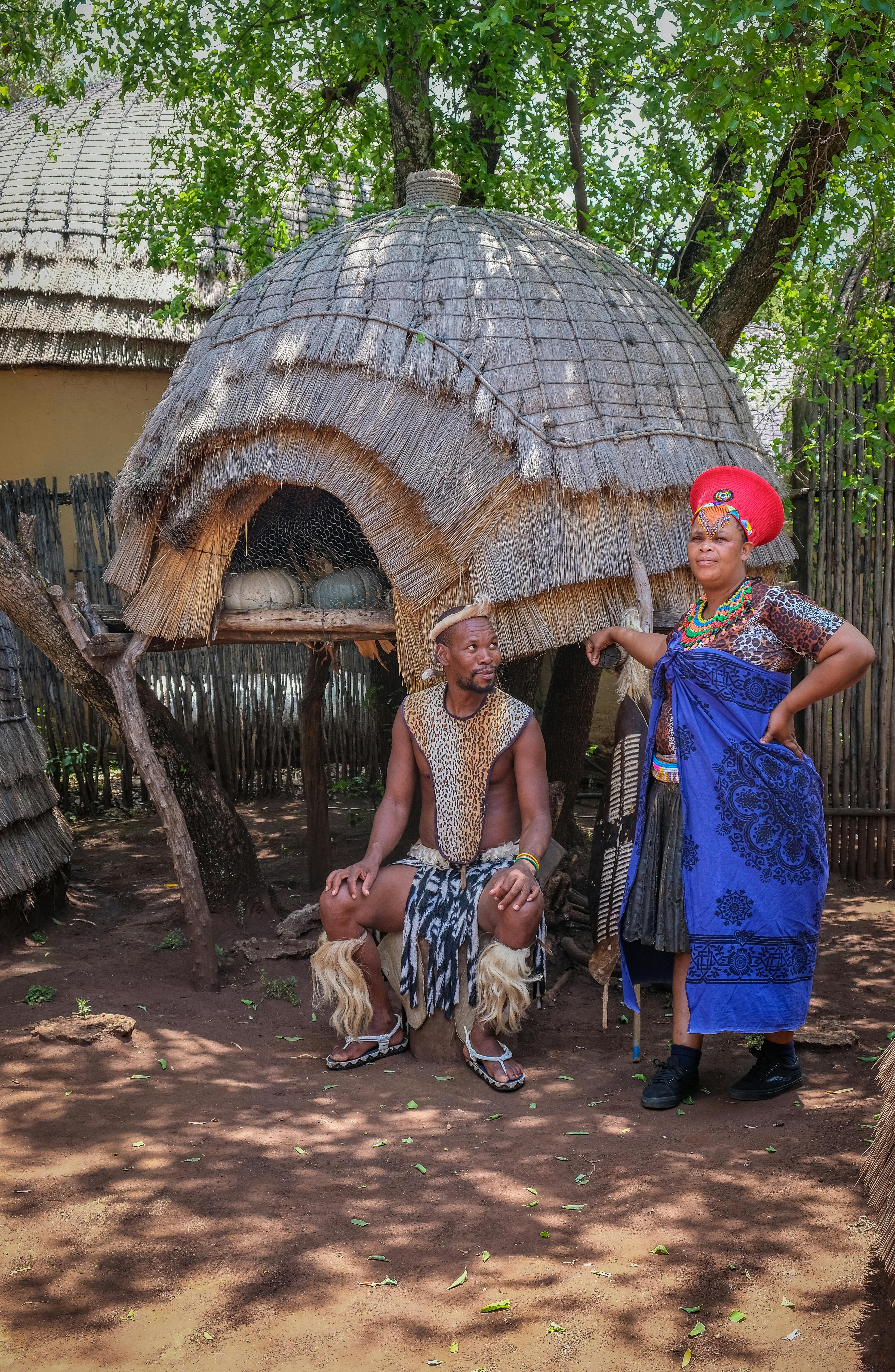 African man and woman in traditional costume posing outside tradtional hut